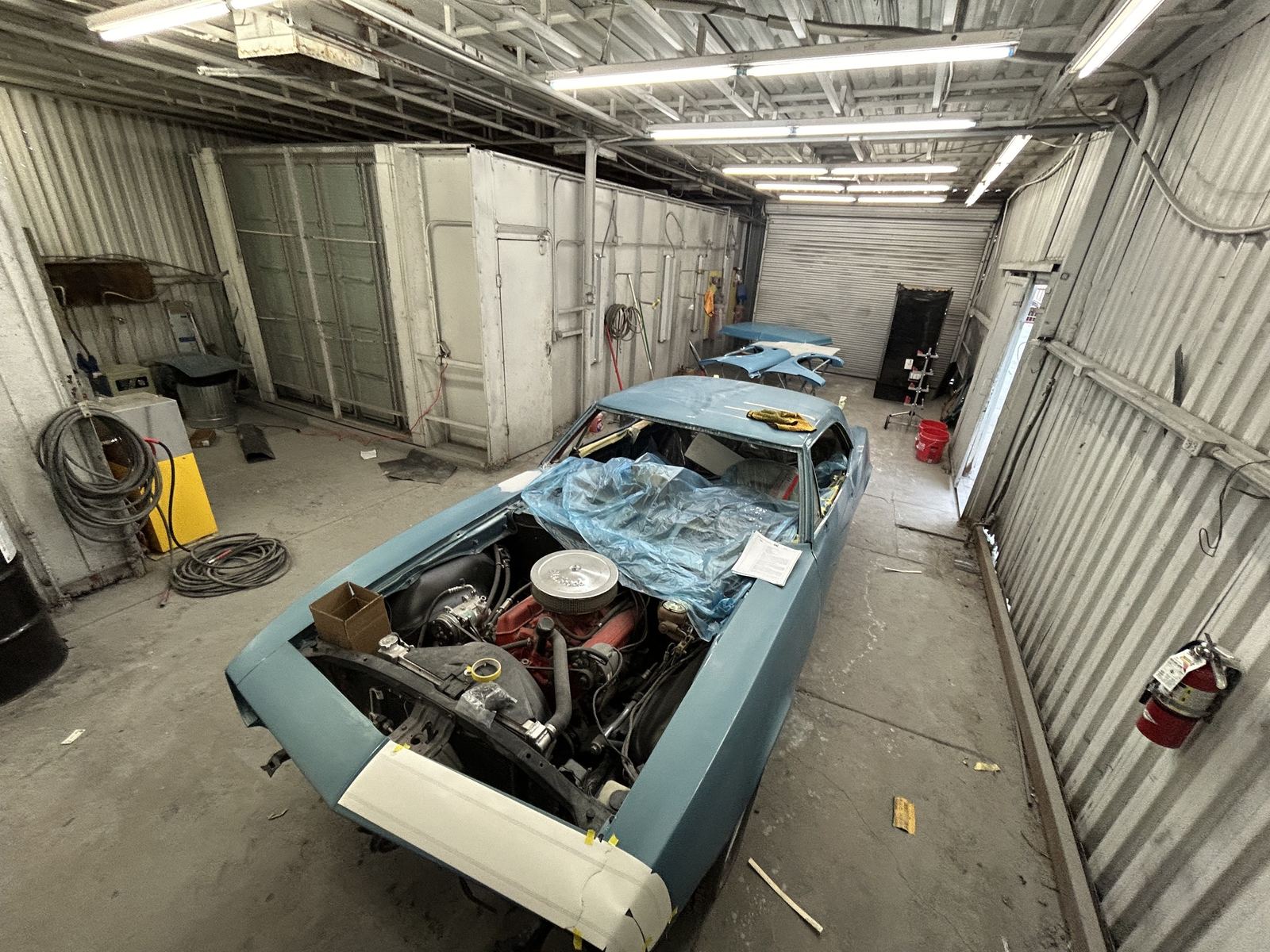 A blue Camaro masked and ready for paint next to the paint booth