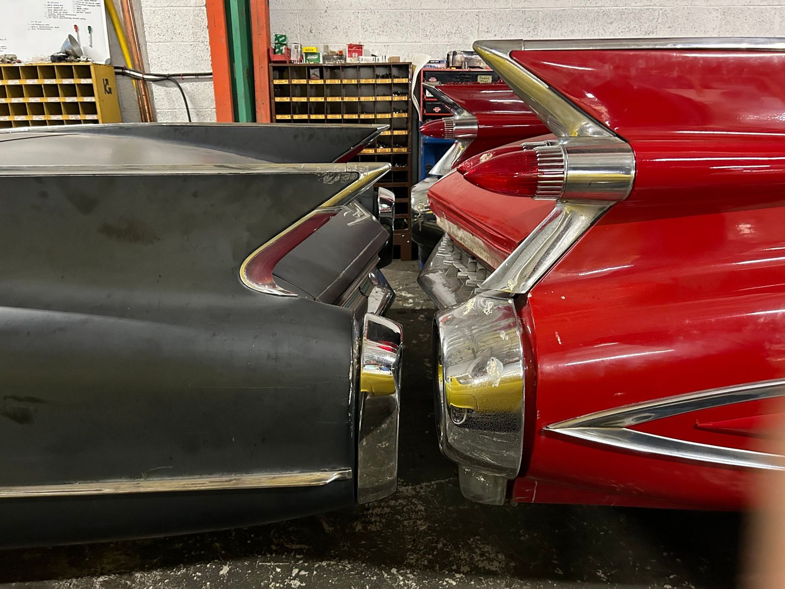 Tail fins of two late 1950s Cadillacs, one in bare metal and one in red, in the shop