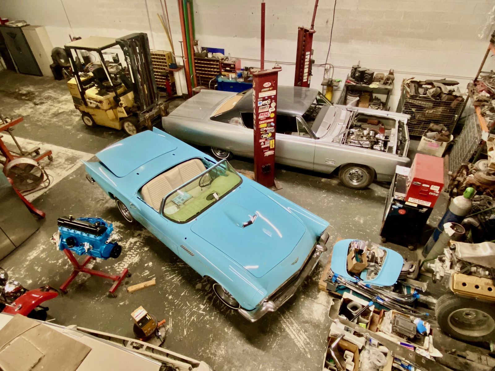 A 1957 Ford Thunderbird with its removable top off, next to a rebuilt engine and a Plymouth Fury in the Phoenix shop